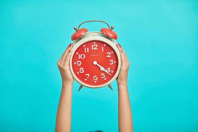 Red alarm clock being held by two hands with a blue background