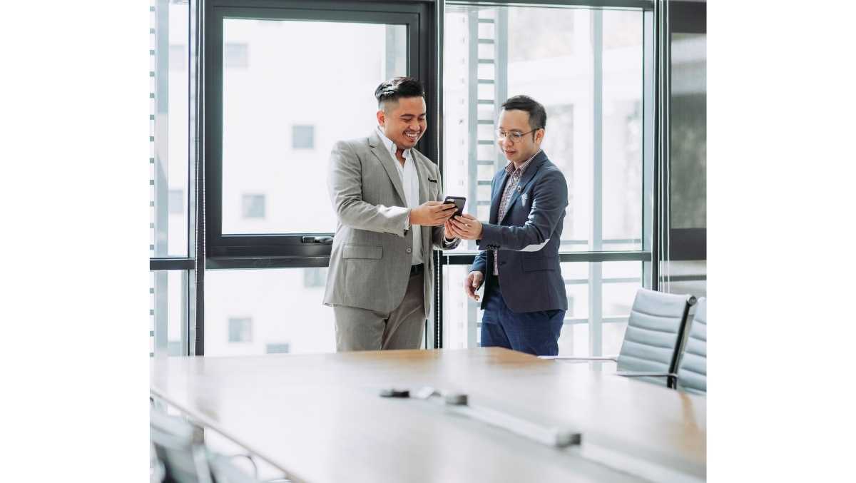 two men in suits looking at a phone in an office space